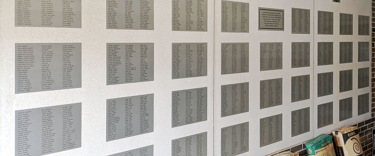 A large concrete rectangle in a brick wall has dozens of smaller metal panels with three columns of names printed on each one.