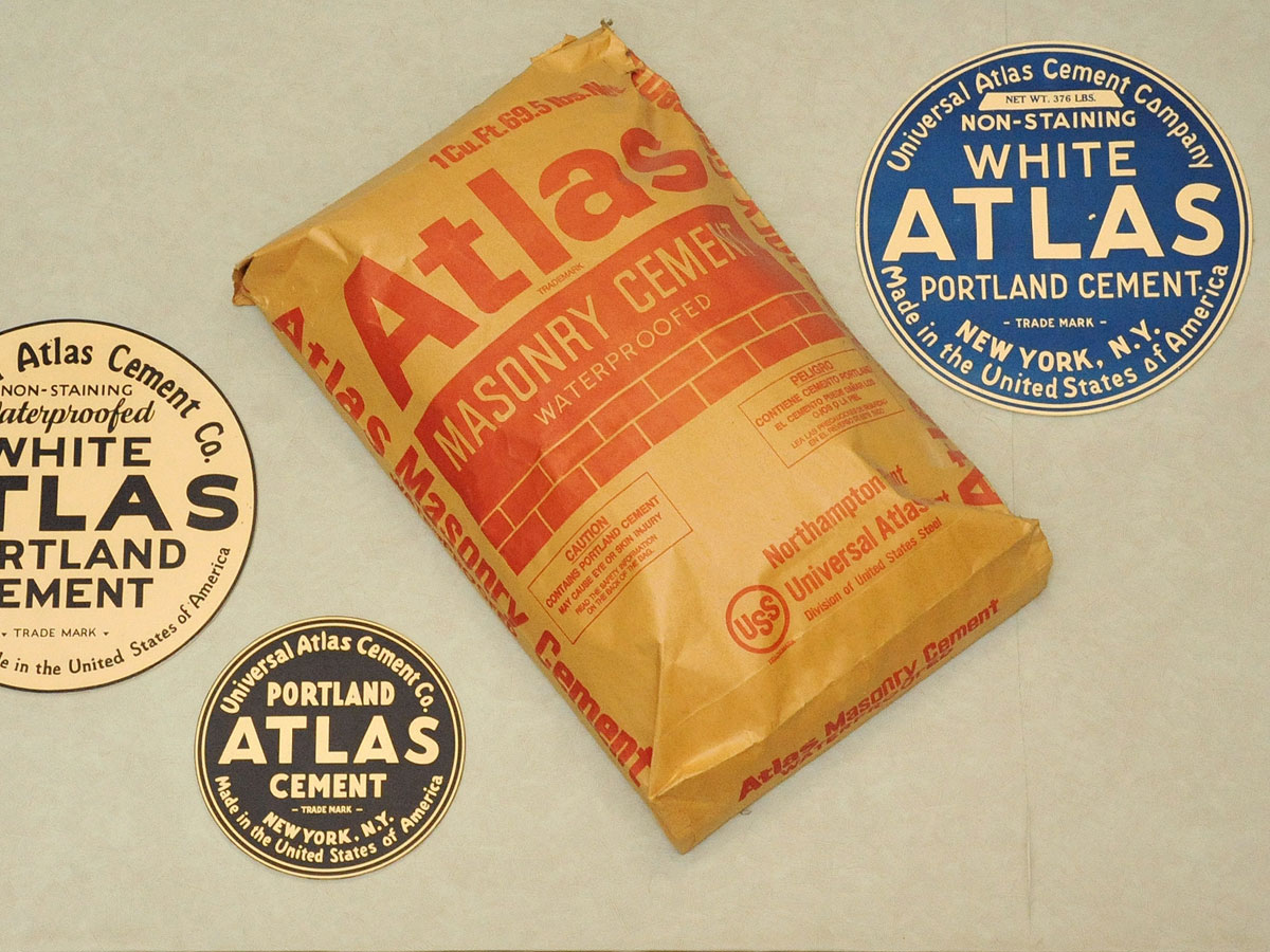 Circular logos of the Atlas Portland Cement Company - in blue, black, and cream colors - alongside a more modern paper sack of Atlas Masonry Cement.